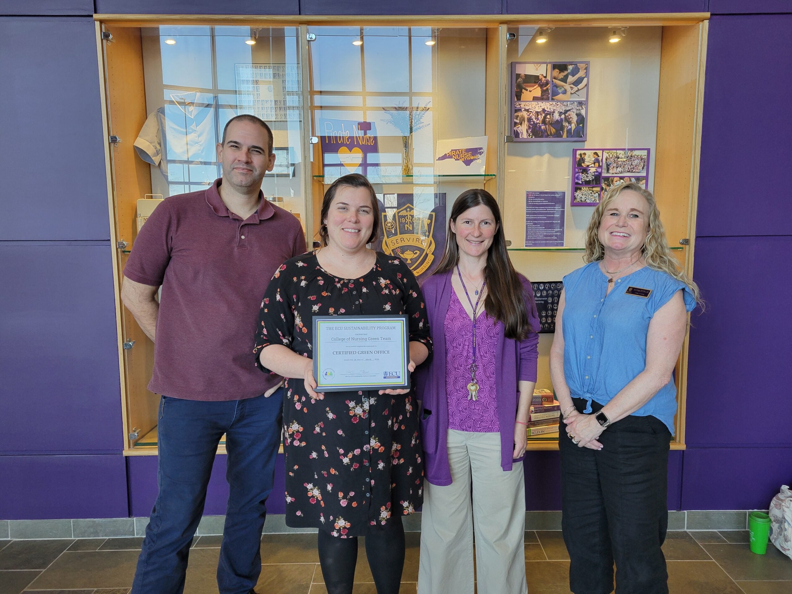 A group of four, the College of Nursing's Green Team, stands together smiling and holding their Green Office Certificate