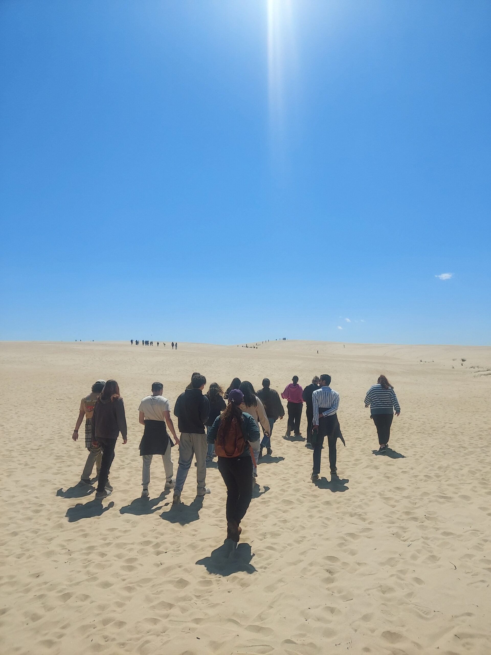 A sandy landscape with a group walking away from the camera towards a sand dune in the distance