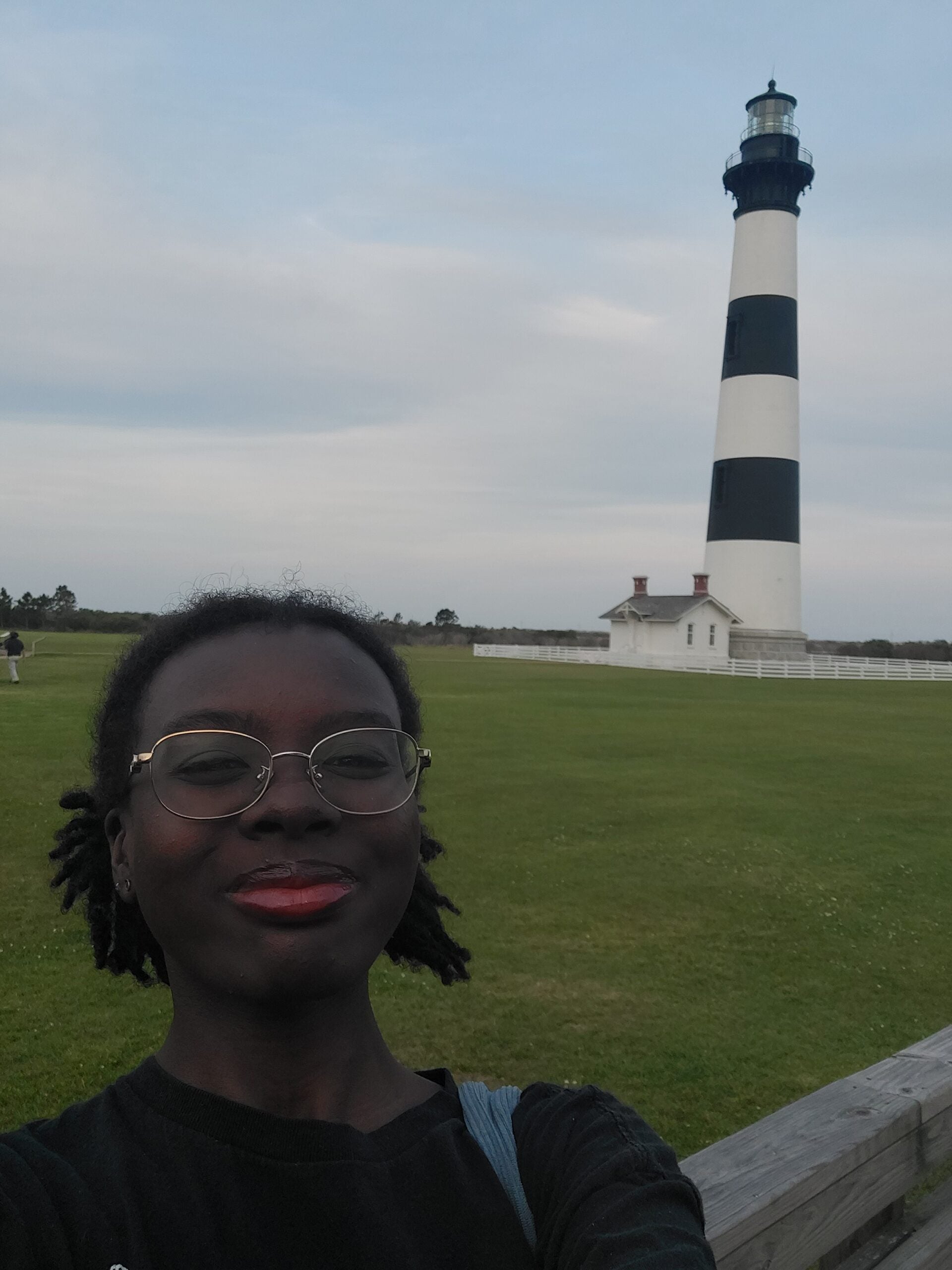 A young woman smiles at the camera with a black and white striped lighthouse in the background