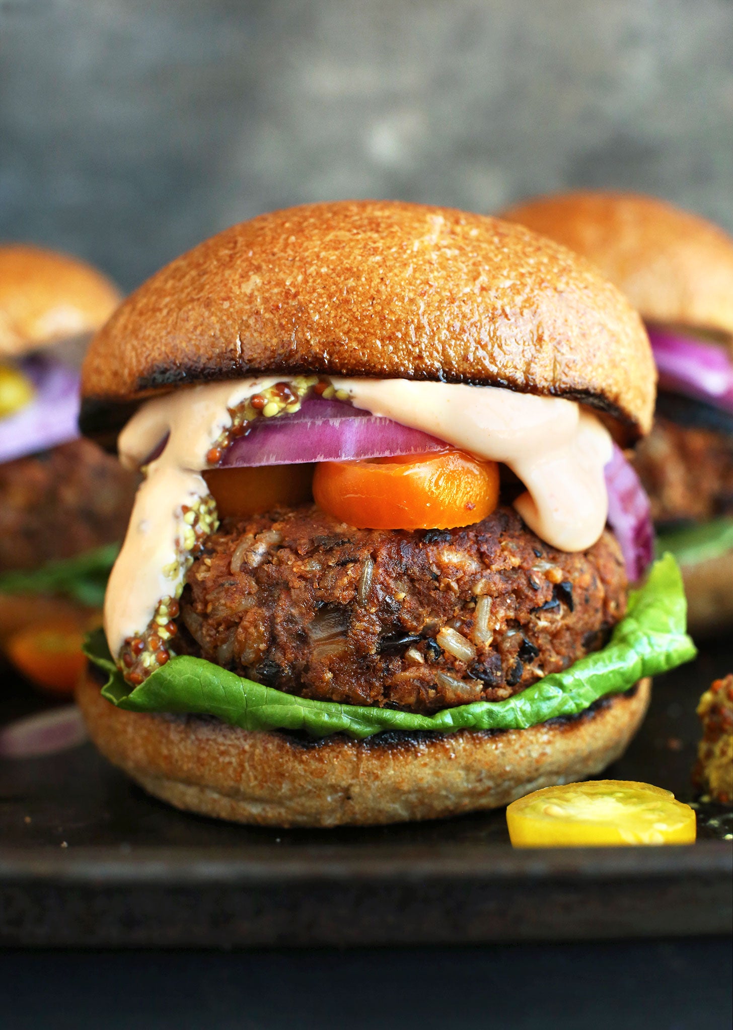 a vegan burger made with black beans, rice, and other vegetables topped with lettuce, onions, peppers, and vegan Sriracha mayo on a bun