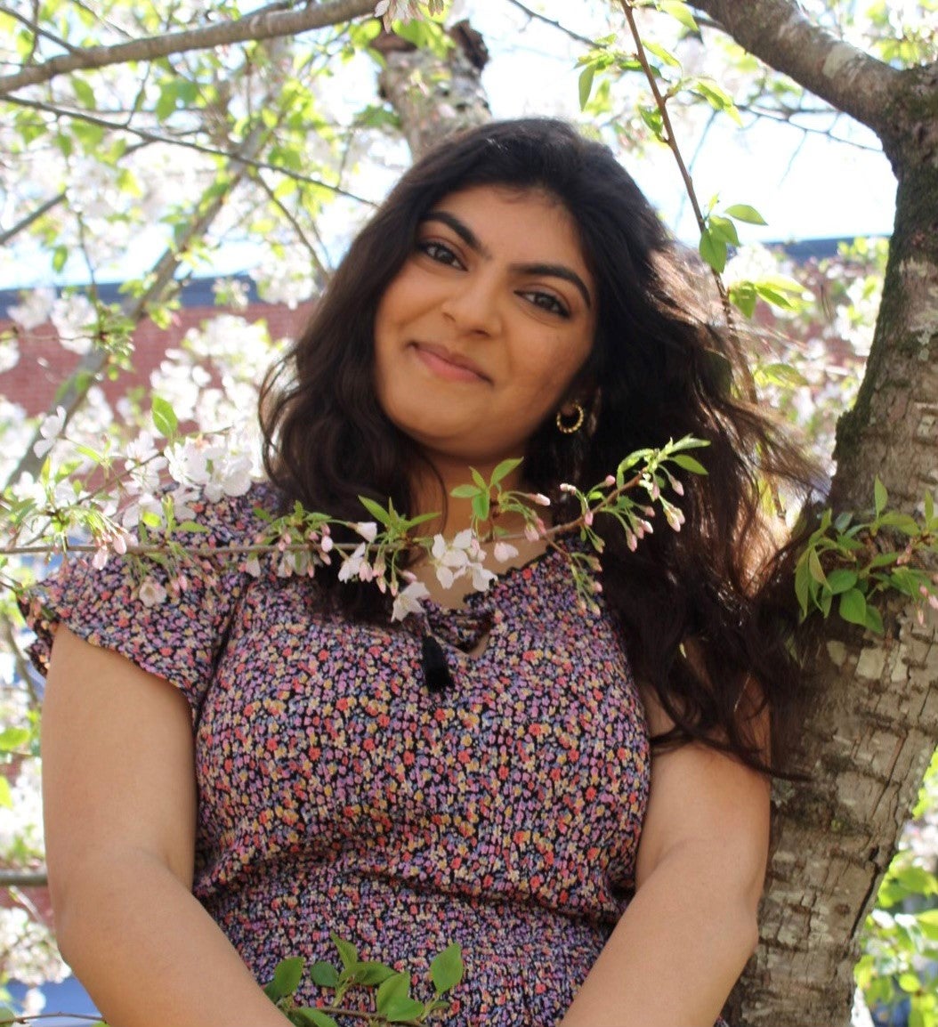 A young woman leans against a flowering tree.