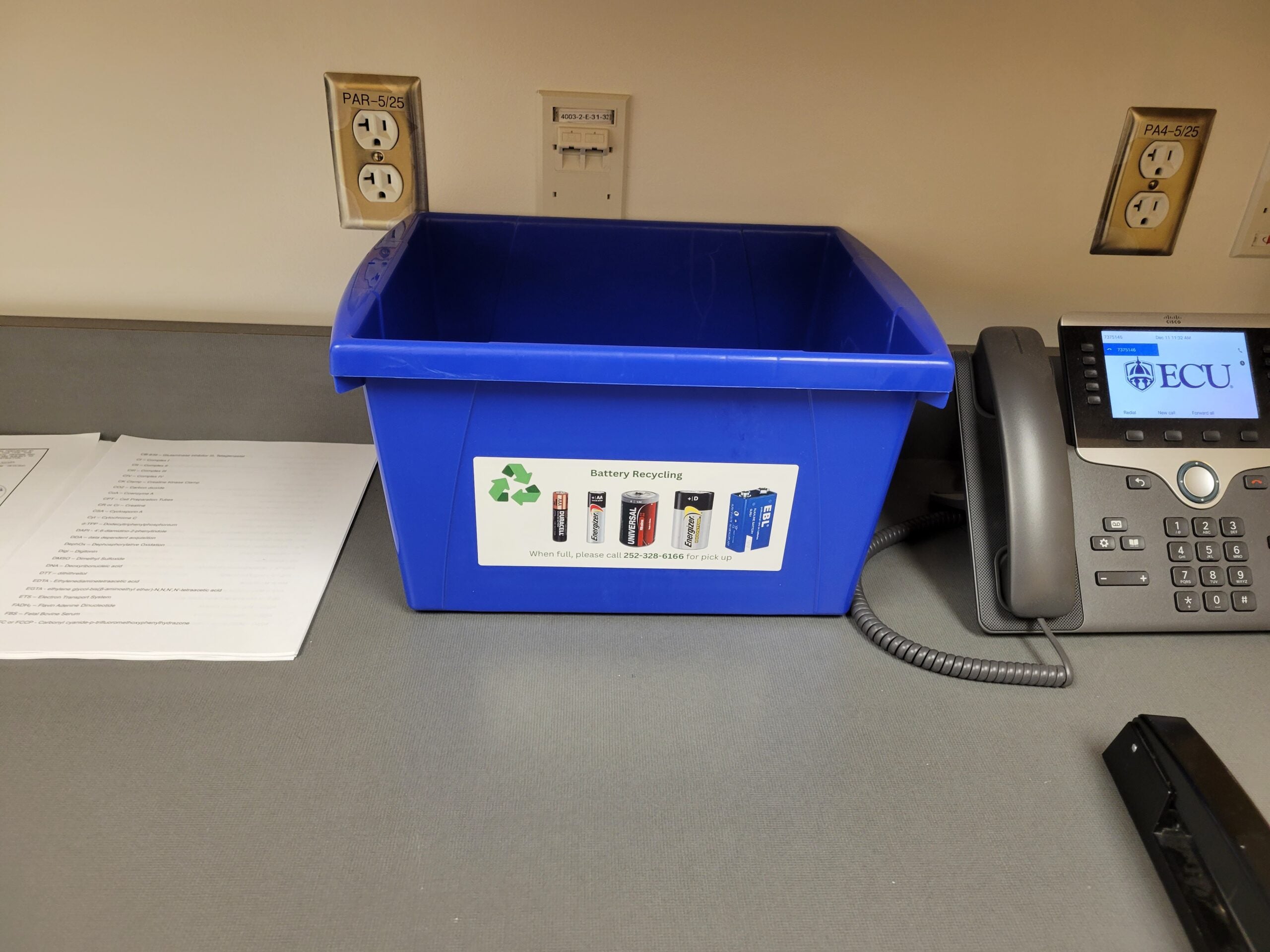 A blue recycling box with pictures of batteries for battery recycling in the office.