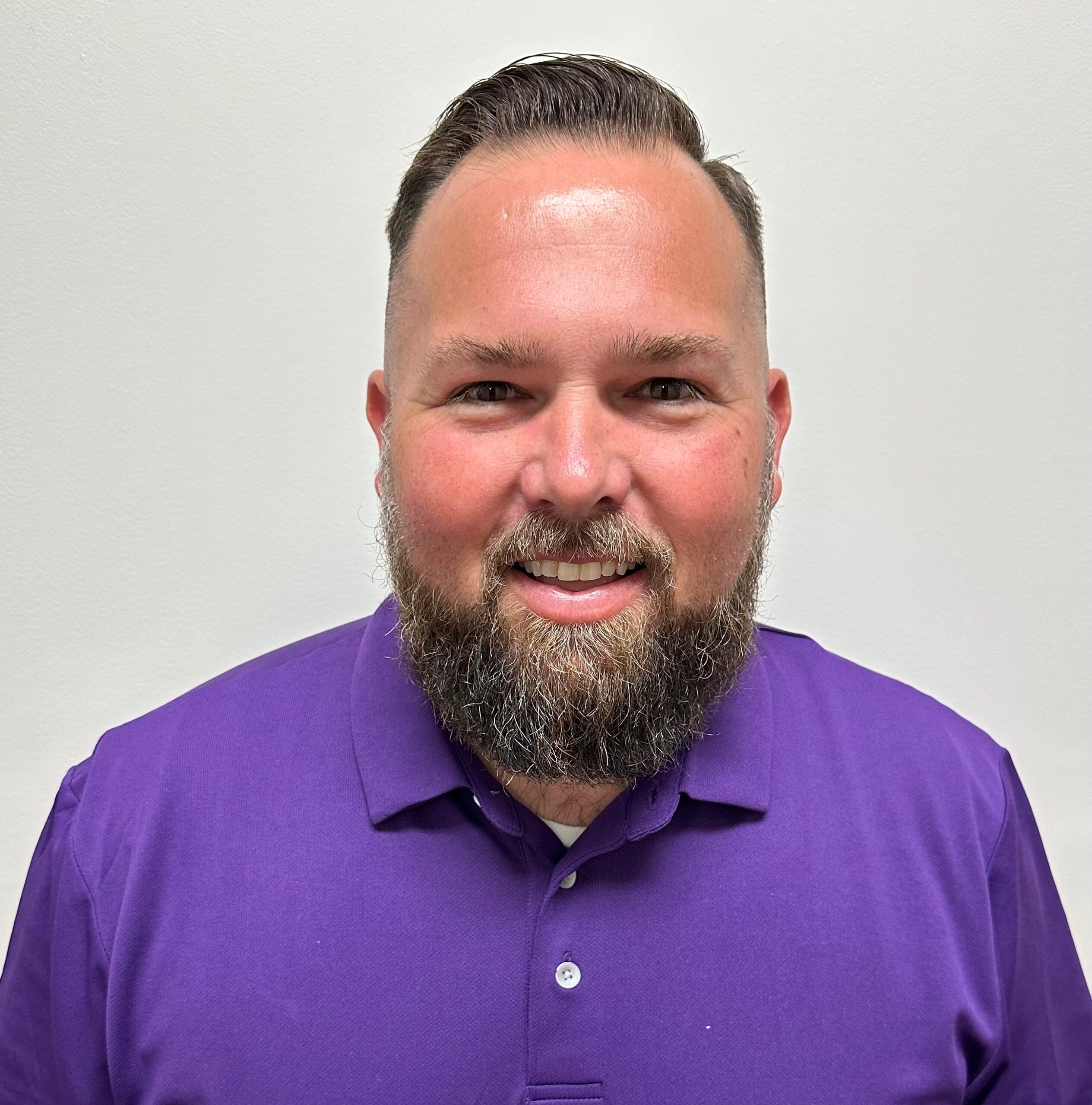 Charles Suggs smiles at the camera, wearing a purple polo