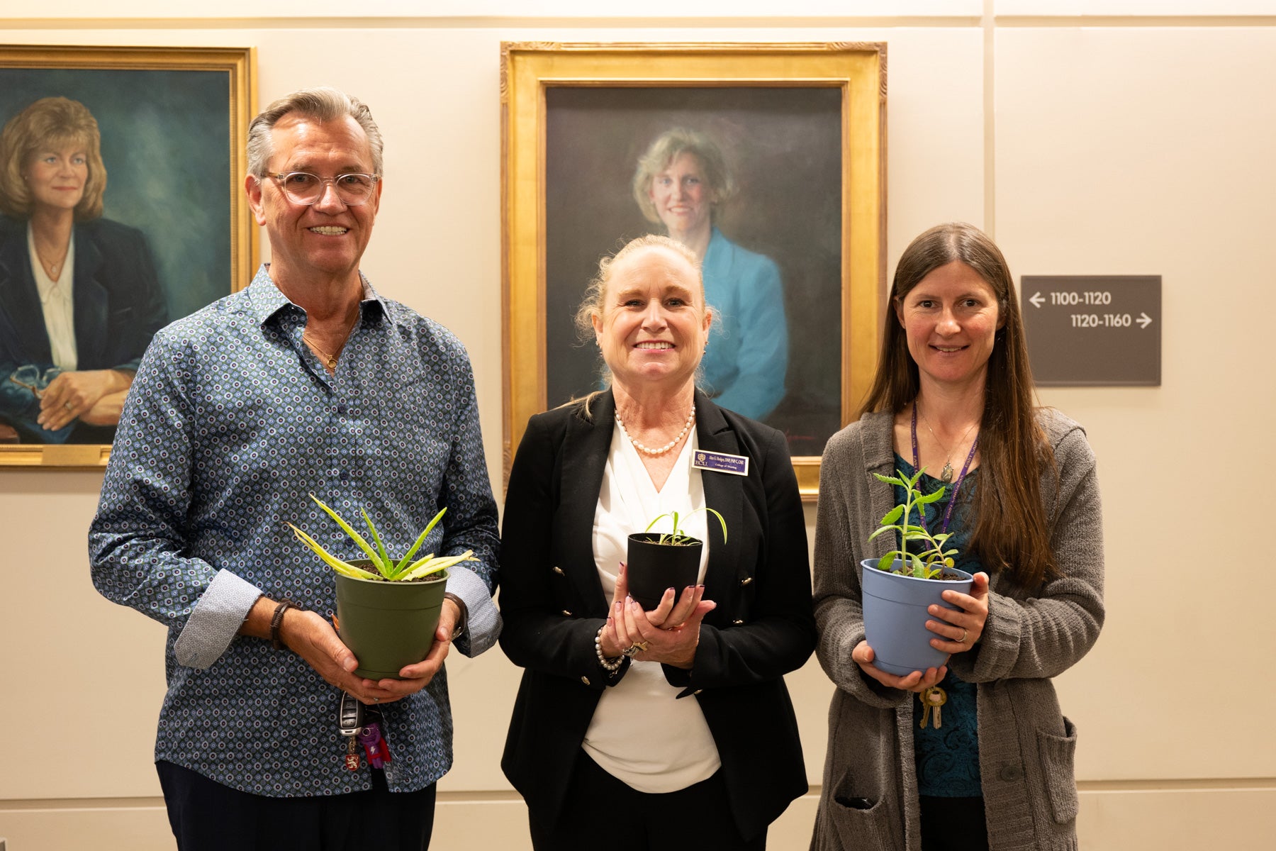 Three members of CON stand smiling and holding plants