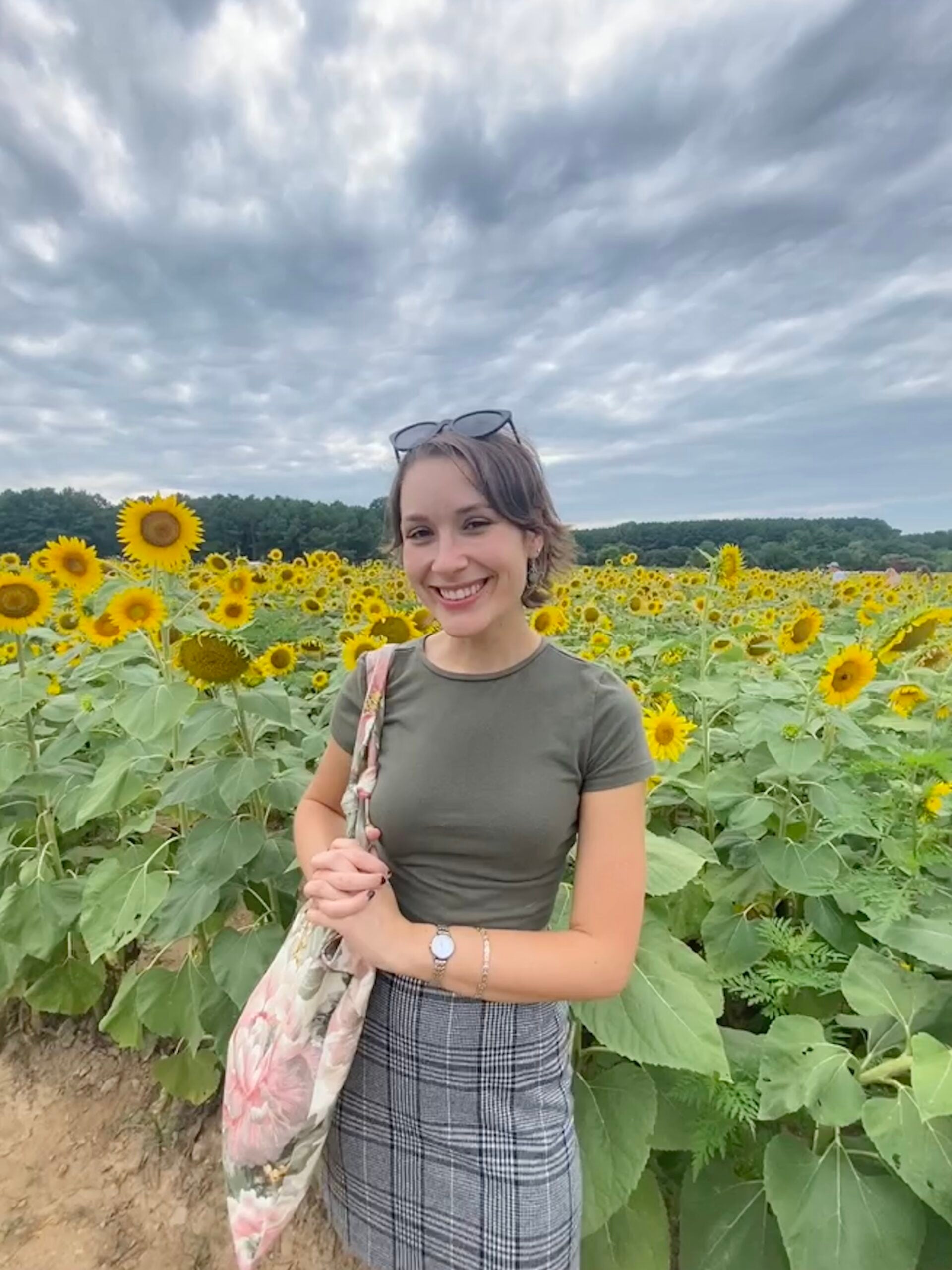 Young woman stands in front of a sunflower field.