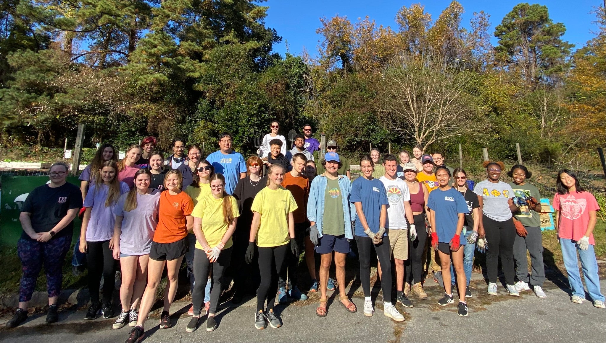 A large group of young adults and teenagers smiling in the community garden