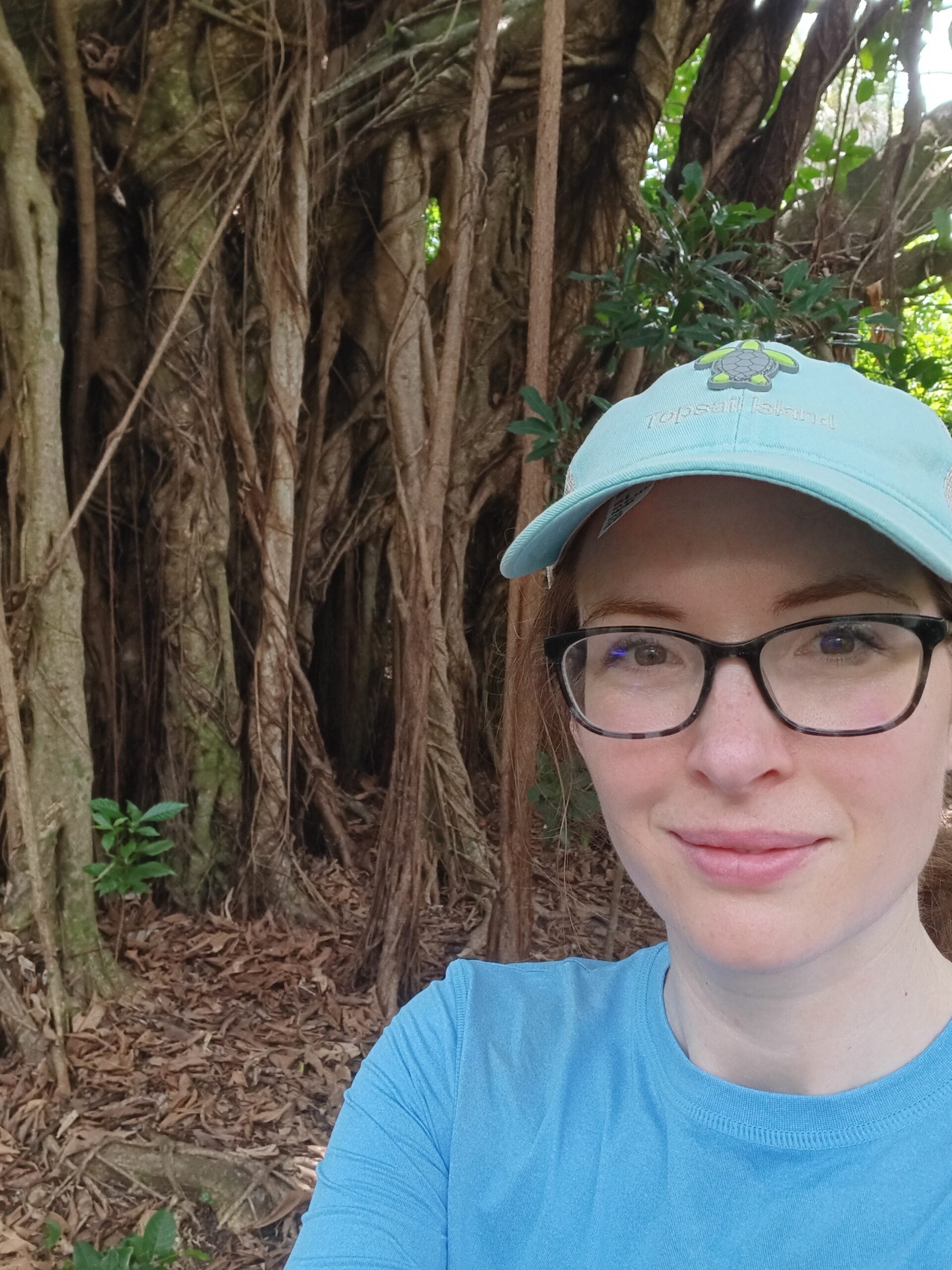 A selfie of Kerry Sewell, a young woman wearing a white baseball cap and glasses, with trees in the background