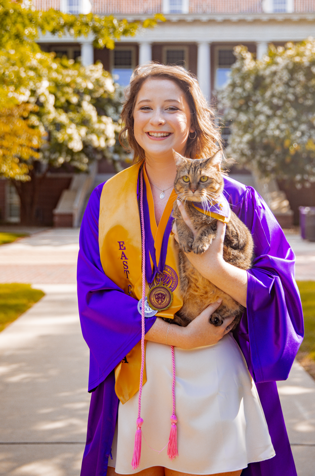 Young woman in purple graduation robes holding a cat.