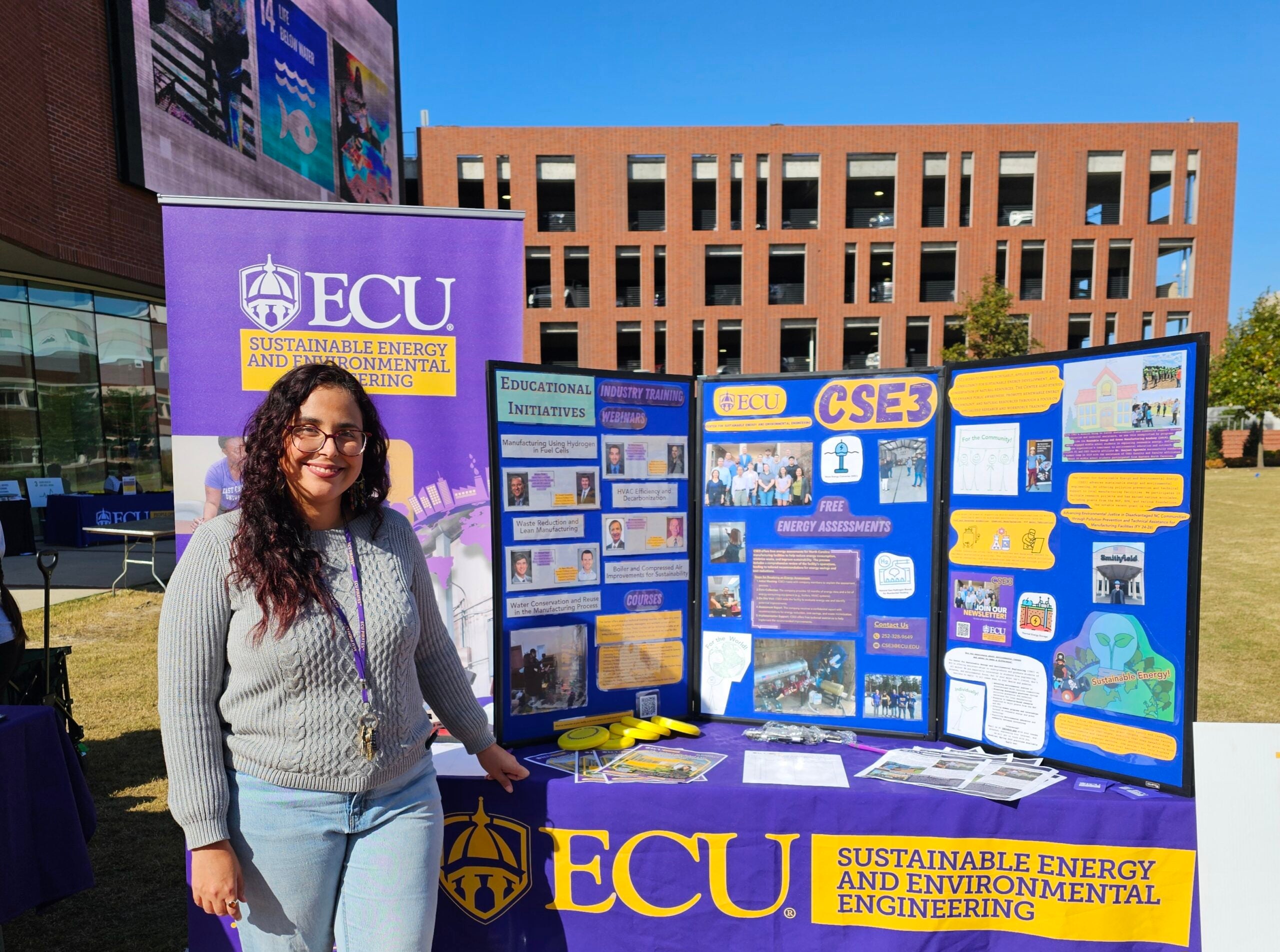 Marly Carmona stands in front of a table with infomation about ECU's Center for Sustainable Energy and Environmental Engineering