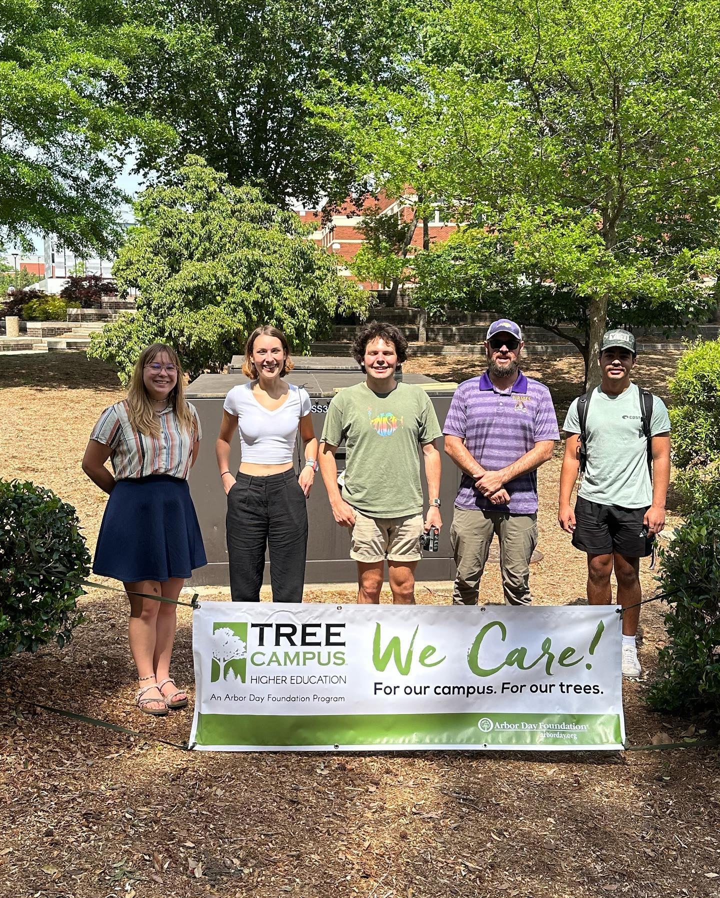 A small group of students stand with Chad Carwein, Sustainability Manager, with a sign proclaiming ECU to be Tree Campus Certified