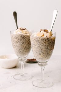 Two glass cups with chia banana pudding and silver spoon in them, links to banana chia pudding recipe