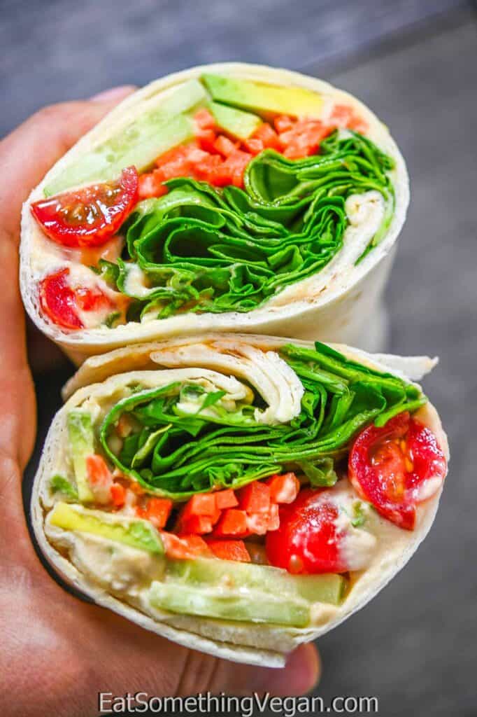 a wrap cut in half to show hummus and a variety of vegetables inside