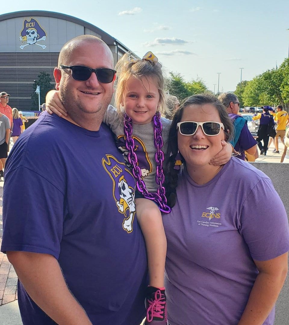 Liz Mizell stands with her husband and daughter at a ECU football game