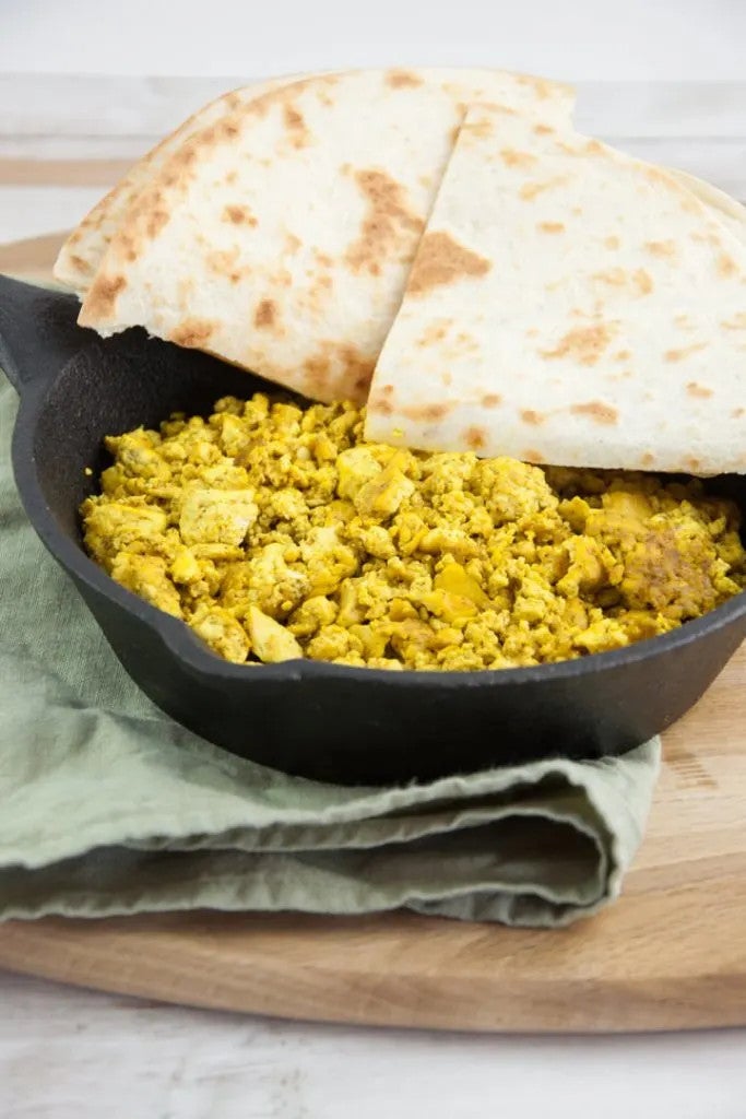 a cast iron pan of what looks like scrambled eggs (it's actually tofu) with two pieces of pita bread on the side